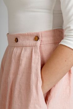 a woman wearing pink pants with buttons on the side and her hands behind her back