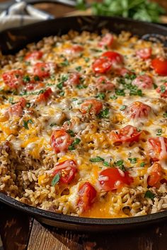 a skillet filled with rice and tomatoes on top of a wooden table next to silverware