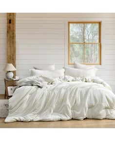 an unmade bed with white sheets and pillows in front of a large window on a wooden floor