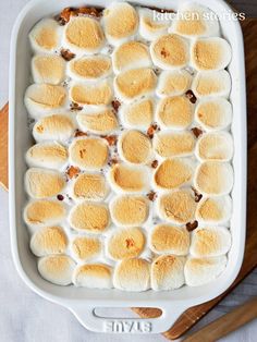 a baking dish filled with marshmallows on top of a wooden cutting board