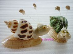 two small ceramic snails sitting on top of each other next to shells with pins stuck in them