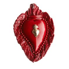 a red heart shaped object hanging from a string on a white wall with beads around it