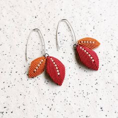 two pairs of earrings with beaded leaves on the end of each earring, sitting on a speckled surface