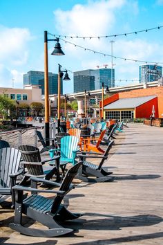 many chairs are lined up on the wooden deck in front of some buildings and lights