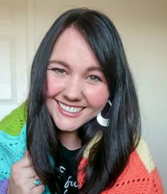 a woman with long black hair wearing a multicolored shawl smiling at the camera