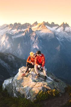 two people sitting on top of a rock in the mountains