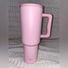 a pink coffee cup sitting on top of a white blanket next to a gray wall