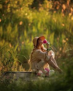 a woman sitting on the ground with a flower in her hand and wearing a hat