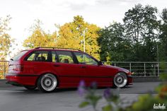 a red car parked in a parking lot next to some trees and bushes on the other side