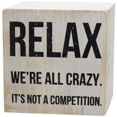 a wooden block that says relax we're all crazy it's not a competition