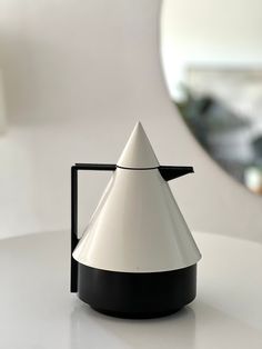 a white and black coffee pot sitting on top of a table next to a mirror