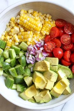 a bowl filled with chopped vegetables and avocado, corn on the cob