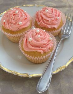 three cupcakes with pink frosting on a plate next to a silver fork