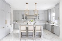 a large kitchen with marble floors and white cabinetry, along with an island table surrounded by beige chairs