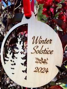 a wooden ornament that says winter solstice in front of red flowers