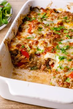 a casserole dish with meat, cheese and vegetables in it on a wooden table