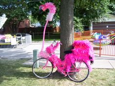 a pink bicycle decorated with feathers is parked next to a tree