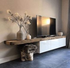 a flat screen tv sitting on top of a wooden shelf next to a vase with flowers