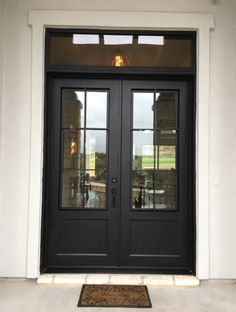 two black double doors with glass panels on the front of a house, and an entrance mat in front of them