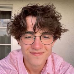 a young man with glasses and a pink shirt is smiling at the camera while standing in front of a house