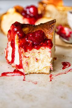 a piece of cheesecake with cranberry sauce on it and some other dessert items in the background