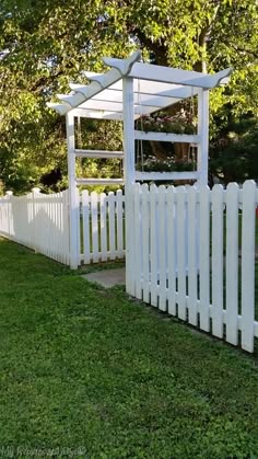 a white picket fence with an arbor in the middle and green grass on both sides