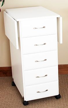 a white filing cabinet with five drawers on casteors and four wheels in front of a wall