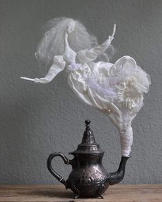 a teapot with a doll in it sitting on top of a table next to a wall