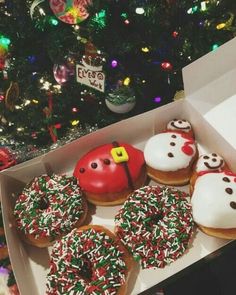 a box filled with donuts covered in frosting and sprinkles next to a christmas tree