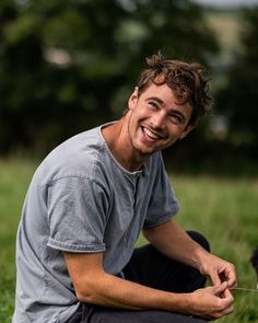 a man sitting in the grass with a toothbrush in his hand and smiling at the camera