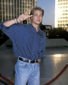 a man in blue shirt and jeans making the peace sign