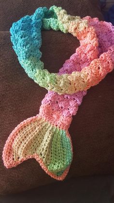 a multicolored crocheted scarf sitting on top of a brown couch next to a pillow