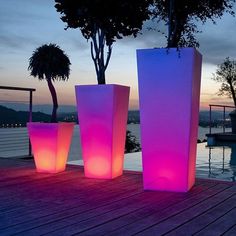 three tall vases sitting on top of a wooden deck next to a lake at night