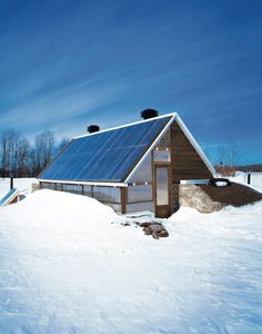 a small house with a solar panel on the roof in the middle of some snow