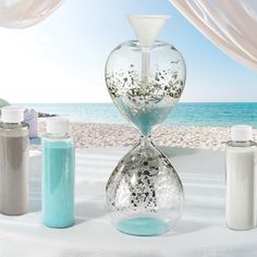 an hourglass sitting on top of a white table next to jars and containers filled with sand