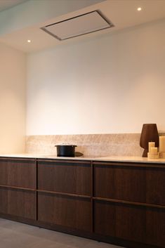 an empty kitchen with wooden cabinets and a black bowl on the counter top in front of a white wall