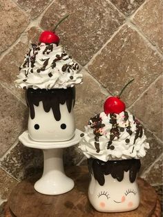 two cupcakes with whipped cream and cherries on top are sitting on a table