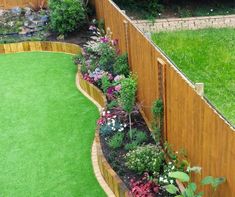 a wooden fence is next to a green lawn with flowers and plants in the corner