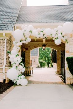 an archway decorated with white balloons and greenery