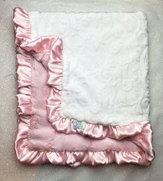 a pink and white blanket laying on top of a floor next to a pillow with ruffled edges