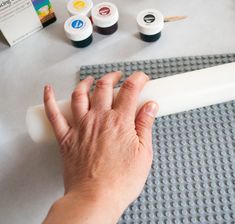 a person's hand on the tip of a white plastic object next to other crafting supplies