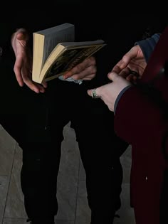 two people holding open books while standing next to each other on the floor with their hands together