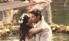 a bride and groom kissing in the water with flowers around them on their wedding day