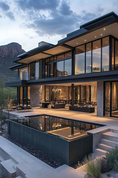 a large modern house with a pool in the front yard at dusk, surrounded by mountains and greenery