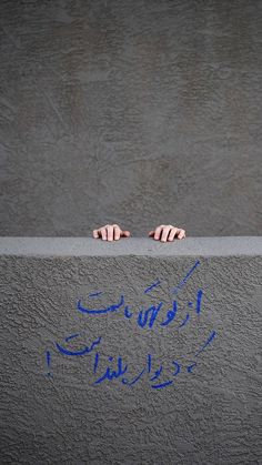 two hands reaching over the edge of a wall with blue writing on it and graffiti