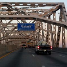 cars are driving on the road under an overpass with a sign that reads kentucky