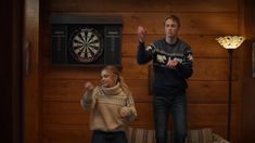 two people standing in front of a wooden wall with darts on the wall behind them