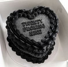 a heart shaped cake in a box with writing on the top and bottom, decorated with black frosting