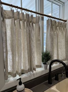 a bathroom with a sink, window curtain and faucet in front of it