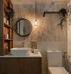 a white toilet sitting next to a bathroom sink under a round mirror on top of a wooden cabinet